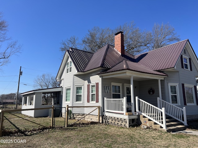 view of front of home featuring metal roof, fence, a chimney, a front yard, and covered porch