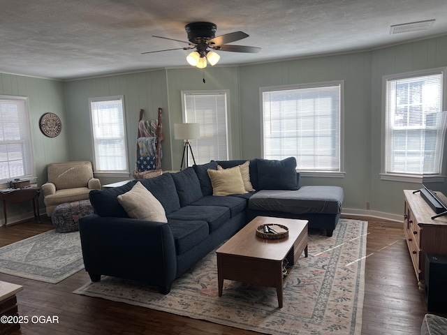 living area with a ceiling fan, a textured ceiling, dark wood-style floors, baseboards, and visible vents