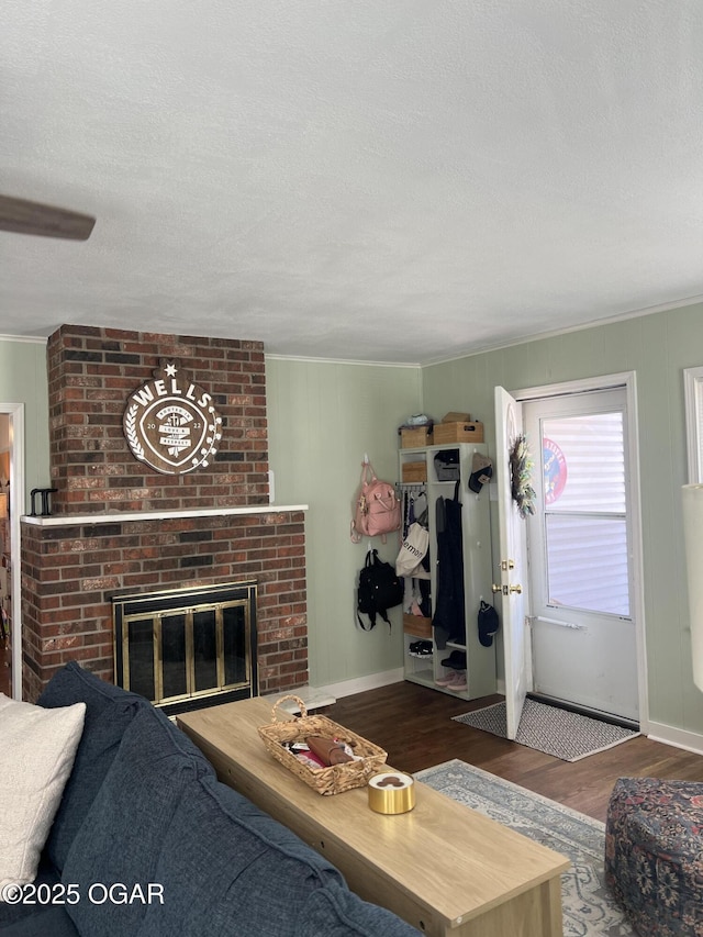 living room with a textured ceiling, crown molding, wood finished floors, and a brick fireplace