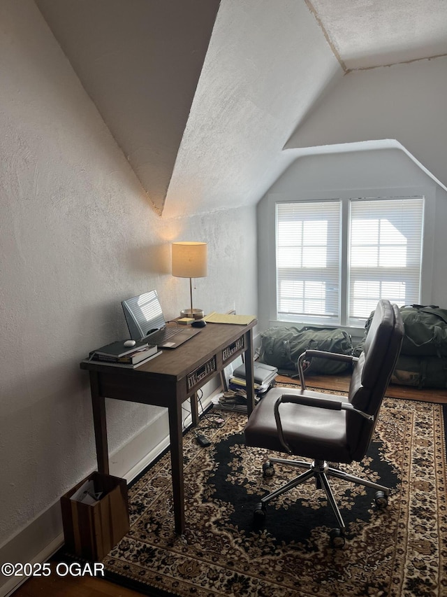 home office featuring a textured wall and vaulted ceiling