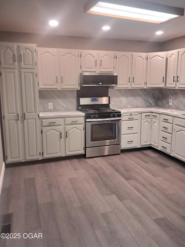 kitchen featuring stainless steel gas stove, wood finished floors, white cabinetry, exhaust hood, and light countertops