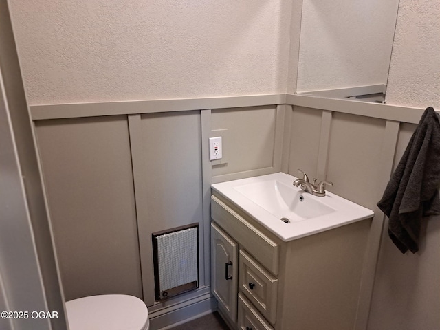 half bathroom with visible vents, toilet, a textured wall, a decorative wall, and vanity