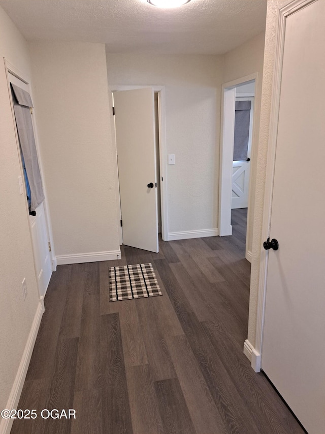 hallway with dark wood-type flooring, baseboards, and a textured ceiling