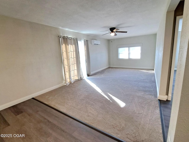 carpeted empty room with ceiling fan, a textured ceiling, a wall mounted air conditioner, and baseboards