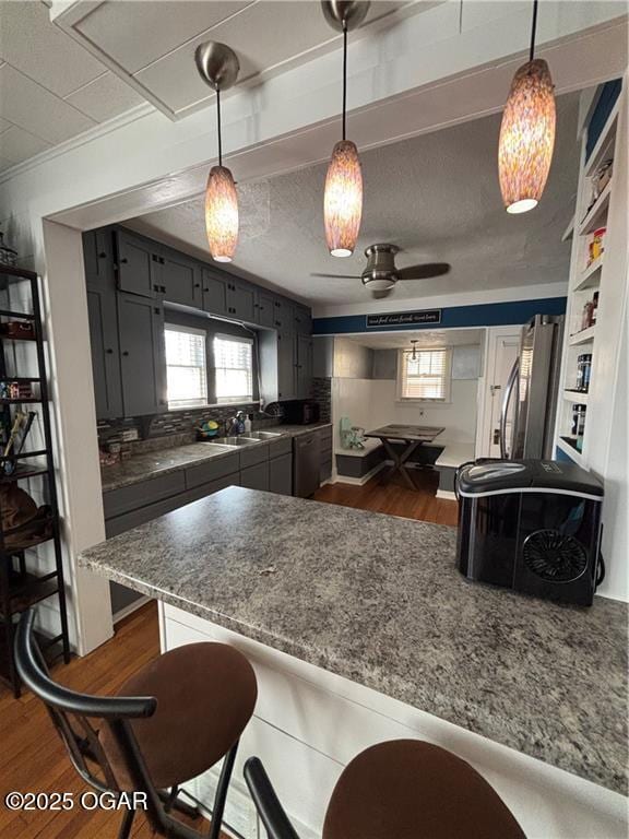 kitchen with dark wood finished floors, a peninsula, a kitchen bar, and a sink