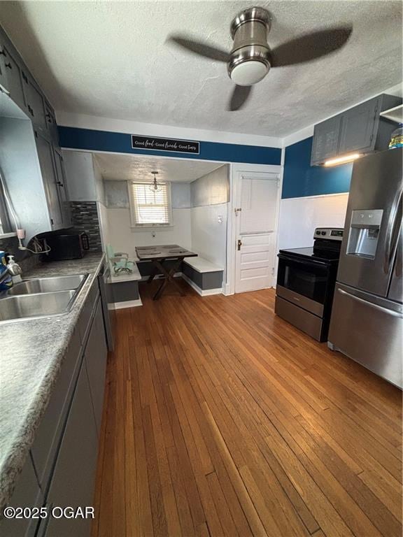 kitchen featuring a ceiling fan, a sink, a textured ceiling, stainless steel appliances, and dark wood-style flooring