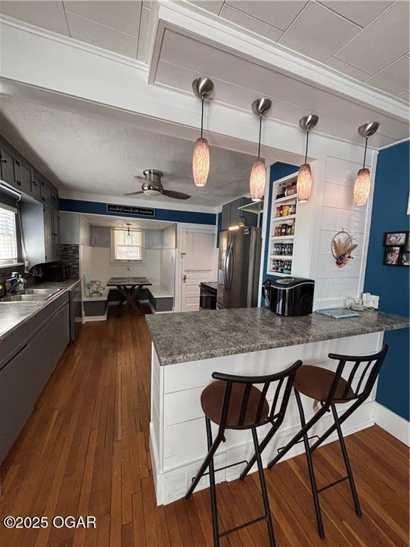 kitchen featuring stainless steel fridge with ice dispenser, a breakfast bar area, a peninsula, dark wood-style floors, and a sink