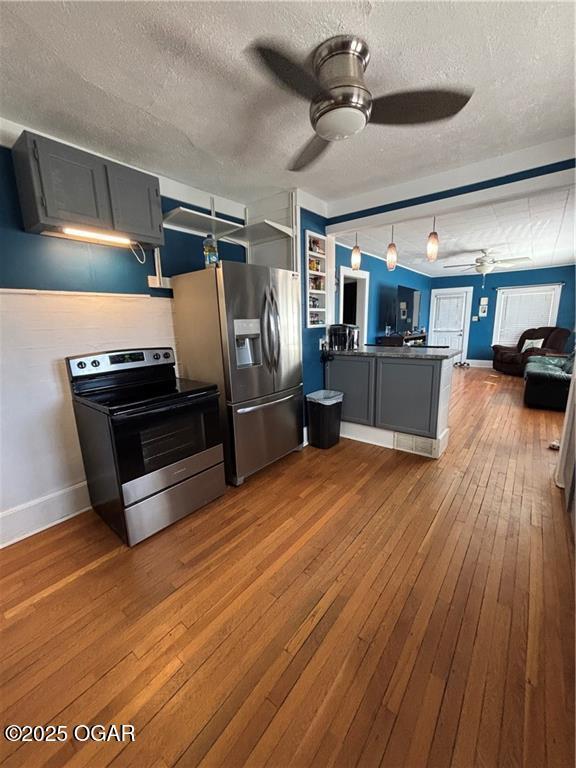 kitchen featuring a peninsula, ceiling fan, stainless steel appliances, dark wood-type flooring, and dark countertops