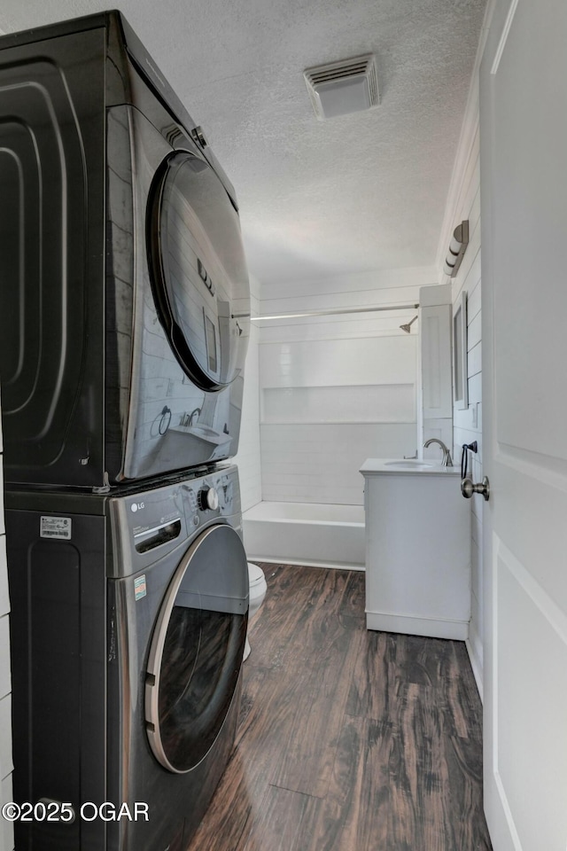 washroom with visible vents, stacked washing maching and dryer, laundry area, dark wood-style flooring, and a textured ceiling