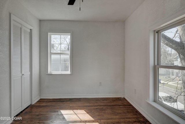 unfurnished bedroom with dark wood finished floors, a closet, baseboards, and a ceiling fan