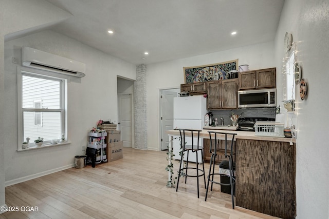 kitchen featuring light wood-type flooring, an AC wall unit, stainless steel microwave, a breakfast bar area, and black range oven