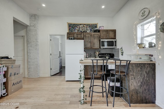 kitchen with freestanding refrigerator, dark brown cabinets, stainless steel microwave, a kitchen breakfast bar, and light wood-type flooring