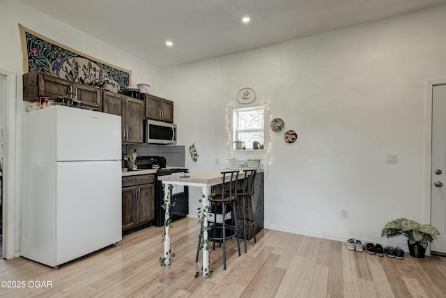 kitchen with freestanding refrigerator, dark brown cabinetry, black range with electric stovetop, stainless steel microwave, and light wood-type flooring