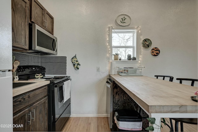 kitchen with stainless steel appliances, dark brown cabinetry, light countertops, light wood-type flooring, and backsplash