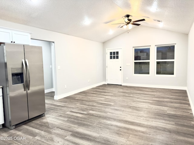 interior space with wood finished floors, visible vents, lofted ceiling, stainless steel fridge with ice dispenser, and white cabinetry