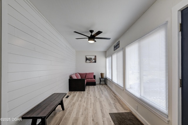 living area with ceiling fan, baseboards, wooden walls, and light wood-style flooring