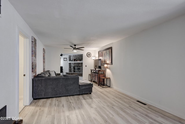 living room featuring visible vents, baseboards, a stone fireplace, light wood-style flooring, and a ceiling fan