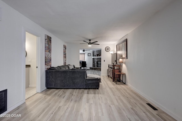 living room with visible vents, light wood-style flooring, a ceiling fan, a fireplace, and baseboards