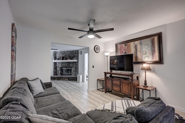 living area with baseboards, a ceiling fan, a fireplace, and light wood finished floors