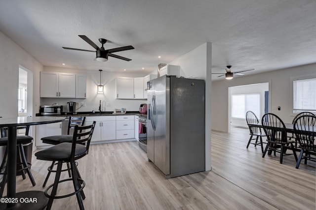 kitchen with stainless steel appliances, dark countertops, white cabinets, and light wood finished floors