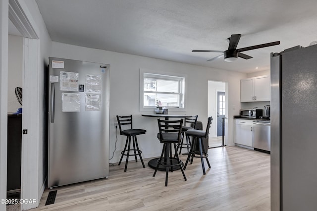 kitchen with ceiling fan, white cabinets, light wood-style floors, appliances with stainless steel finishes, and dark countertops