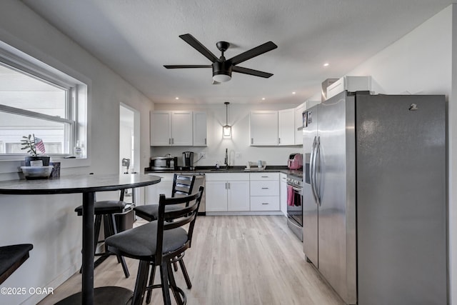 kitchen with light wood-style flooring, a sink, dark countertops, appliances with stainless steel finishes, and white cabinets