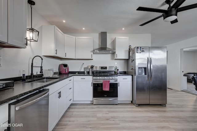 kitchen featuring a ceiling fan, a sink, stainless steel appliances, wall chimney exhaust hood, and light wood-type flooring