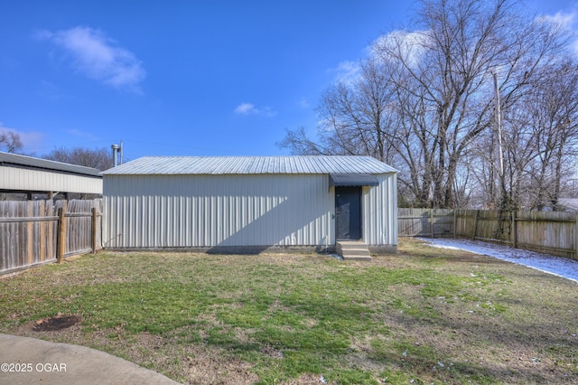 rear view of house with a yard, an outbuilding, metal roof, and a fenced backyard