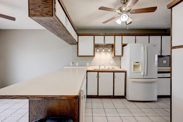 kitchen with a sink, white fridge with ice dispenser, ceiling fan, and light countertops