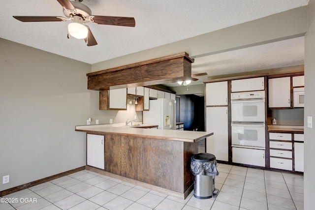 kitchen with white appliances, a peninsula, light countertops, white cabinets, and a textured ceiling