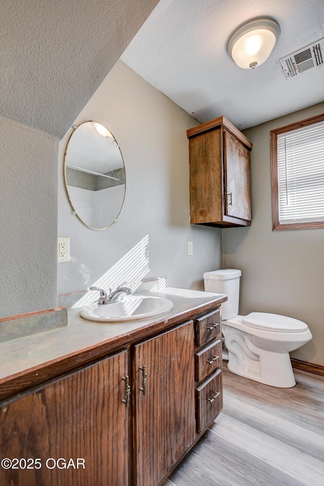 bathroom with vanity, wood finished floors, visible vents, a textured ceiling, and toilet