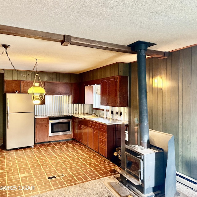 kitchen featuring light countertops, freestanding refrigerator, wood walls, a wood stove, and wall oven