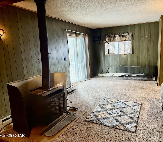 interior space with carpet floors, wooden walls, a wood stove, and a textured ceiling