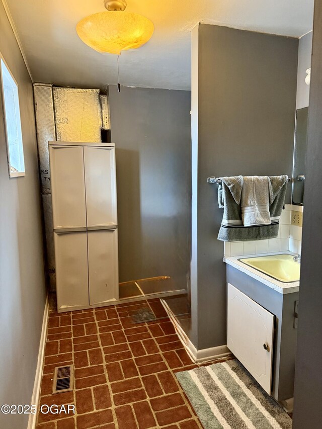 kitchen featuring a sink, brick floor, baseboards, and visible vents