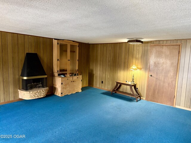 interior space featuring a fireplace, wood walls, a textured ceiling, baseboards, and carpet