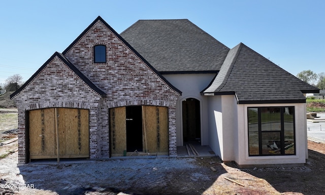 view of front of property featuring brick siding, a shingled roof, and stucco siding