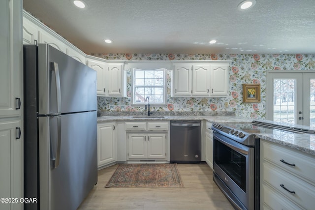 kitchen featuring light stone countertops, wallpapered walls, a sink, stainless steel appliances, and white cabinets