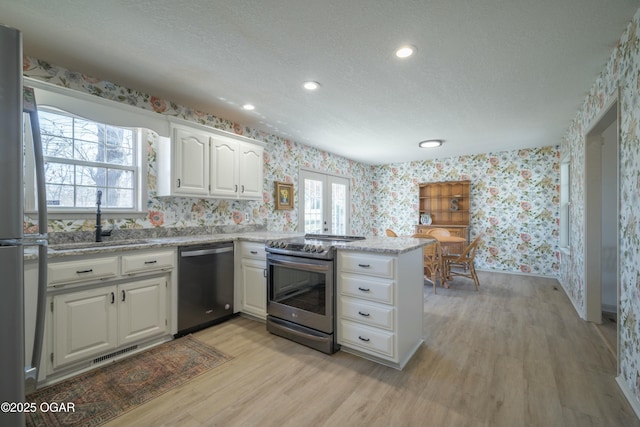 kitchen with wallpapered walls, a peninsula, plenty of natural light, a sink, and appliances with stainless steel finishes