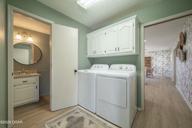 washroom with wallpapered walls, cabinet space, separate washer and dryer, light wood-style floors, and a textured ceiling