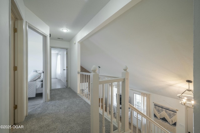 corridor featuring an inviting chandelier, carpet flooring, and an upstairs landing