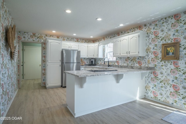 kitchen with white cabinetry, a peninsula, freestanding refrigerator, and wallpapered walls