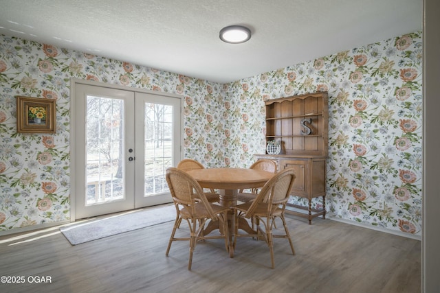 dining room with wallpapered walls, baseboards, french doors, wood finished floors, and a textured ceiling