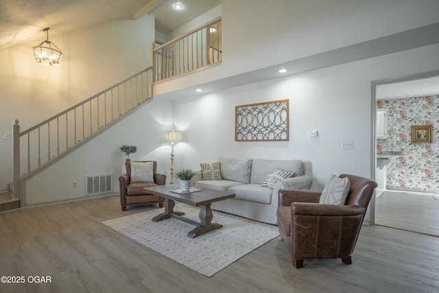 living room featuring stairway, wood finished floors, visible vents, baseboards, and a high ceiling