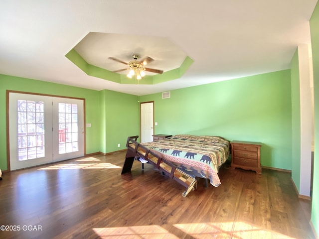 bedroom with wood finished floors, visible vents, baseboards, access to exterior, and a raised ceiling