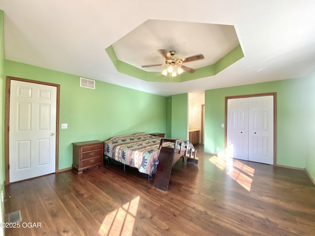 bedroom featuring a tray ceiling, wood finished floors, visible vents, and baseboards