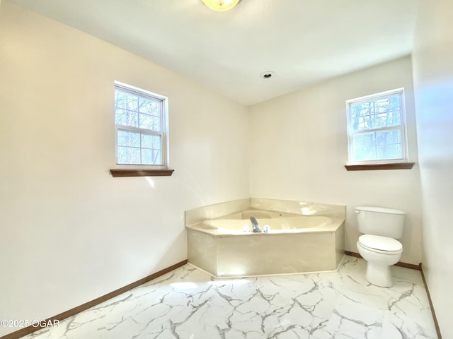 bathroom with a garden tub, plenty of natural light, baseboards, and marble finish floor