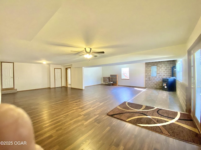 unfurnished living room featuring baseboards, a wood stove, ceiling fan, and wood finished floors