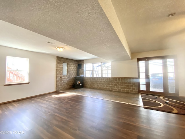 unfurnished living room with visible vents, baseboards, a wood stove, wood finished floors, and a textured ceiling