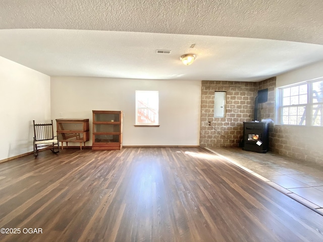 unfurnished room with visible vents, a textured ceiling, a wood stove, and wood finished floors