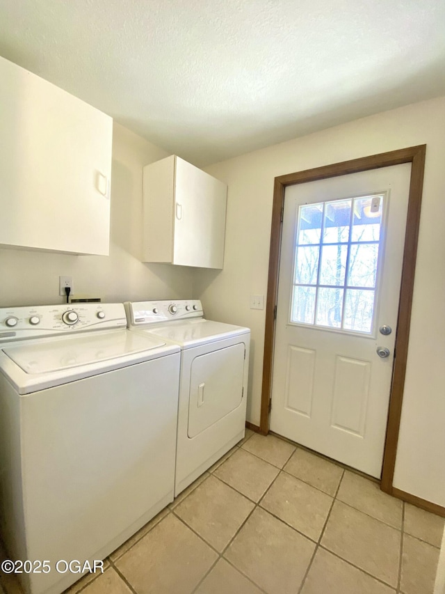 laundry room with a textured ceiling, washing machine and dryer, cabinet space, light tile patterned floors, and baseboards